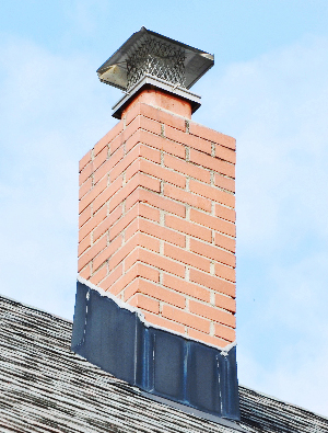 A red brick chimney on top of a gray shingle roof.