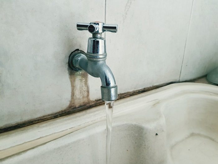 A close-up of a running faucet with water stains on the wall.