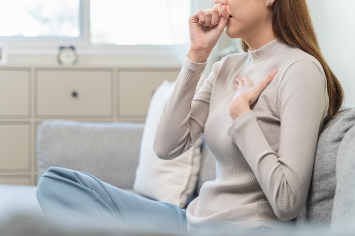 A woman coughs and holds a hand to her chest.